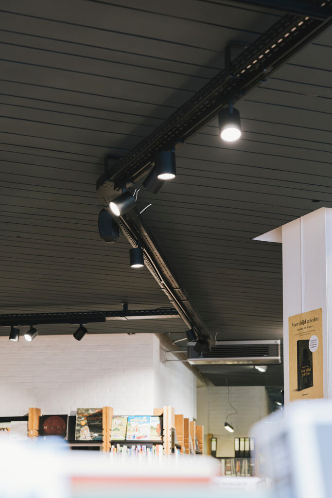 verlichte zwarte spots aan plafond in winkel of bibliotheek met boekenplanken en poster aan muur