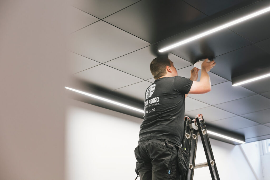 elektricien van electro pacco monteert lichtarmatuur aan modern zwart plafond op ladder