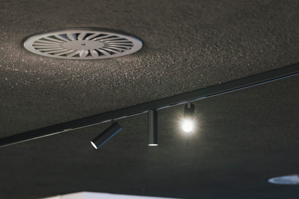 zwarte plafondspots en ronde ventilatierooster in een moderne binnenruimte
