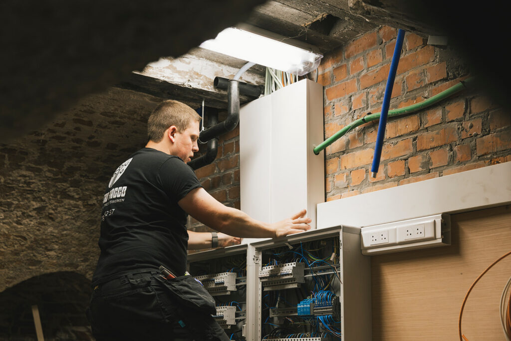 elektricien van electro pacco werkt aan verdeelkast in kelder met bakstenen muren