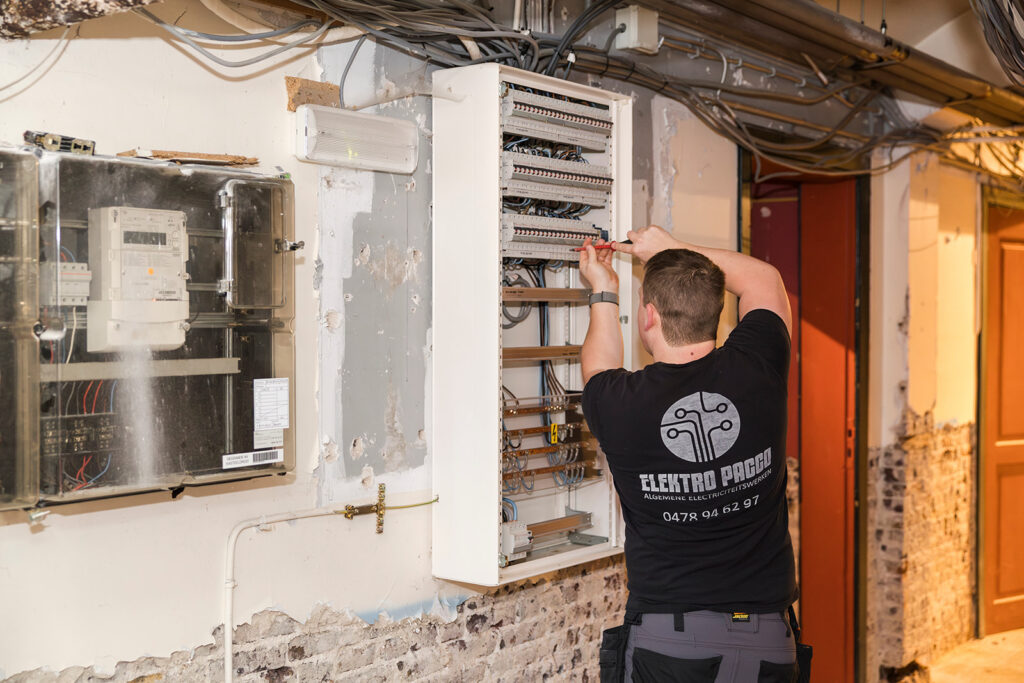 elektricien van elektro pacco werkt in meterkast in oude gevel met zichtbare kabels en schakelaars
