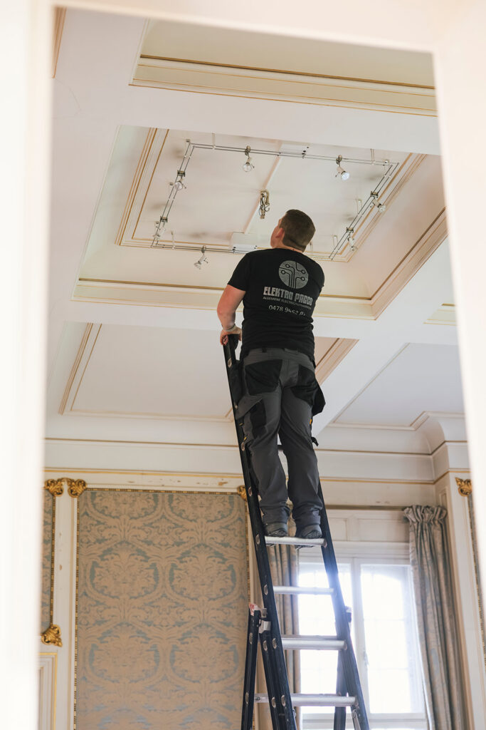 elektricien van electro pacco op ladder bezig met verlichting aan plafond in klassieke kamer