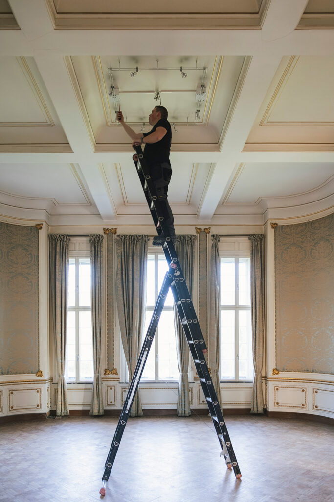elektricien van electro pacco op ladder die verlichting installeert in luxe kamer met hoge plafonds