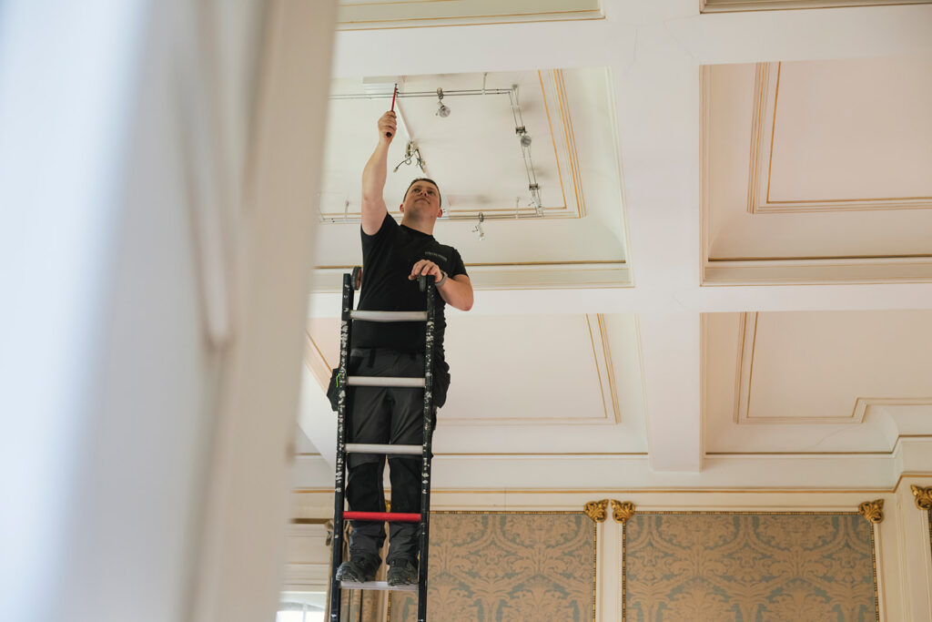 elektricien van electro pacco op ladder monteert verlichting aan sierplafond