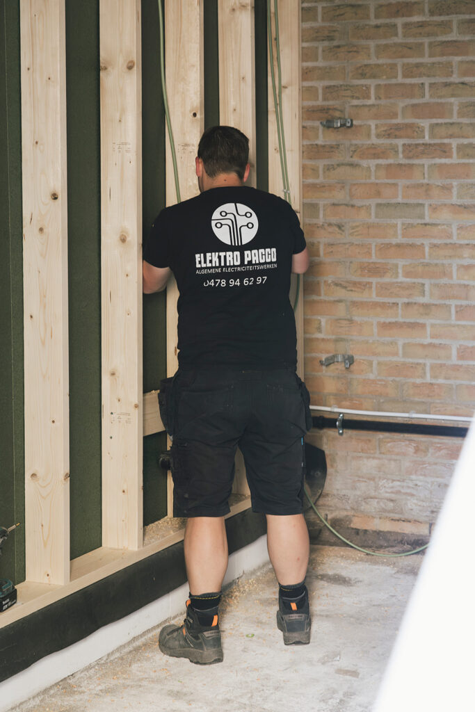 elektricien van electro pacco werkt aan bedrading tegen houten muur in renovatieproject