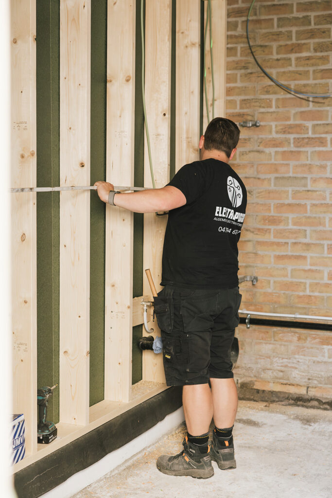elektricien van electro pacco meet houten frame bij bouwproject in zedelgem