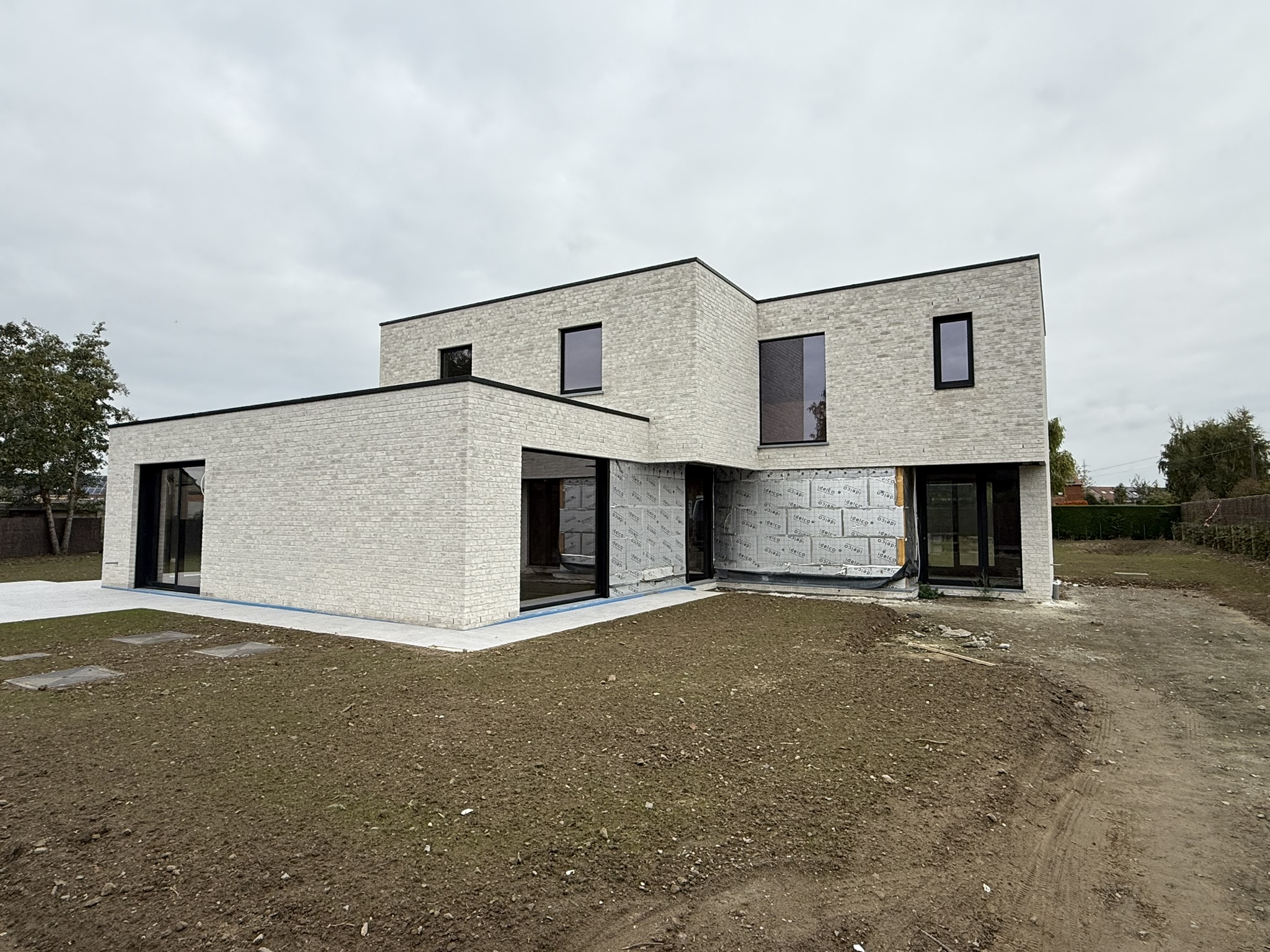 moderne kubistische witte nieuwbouwwoning in afwerking met grote ramen en kale tuin electro pacco zedelgem